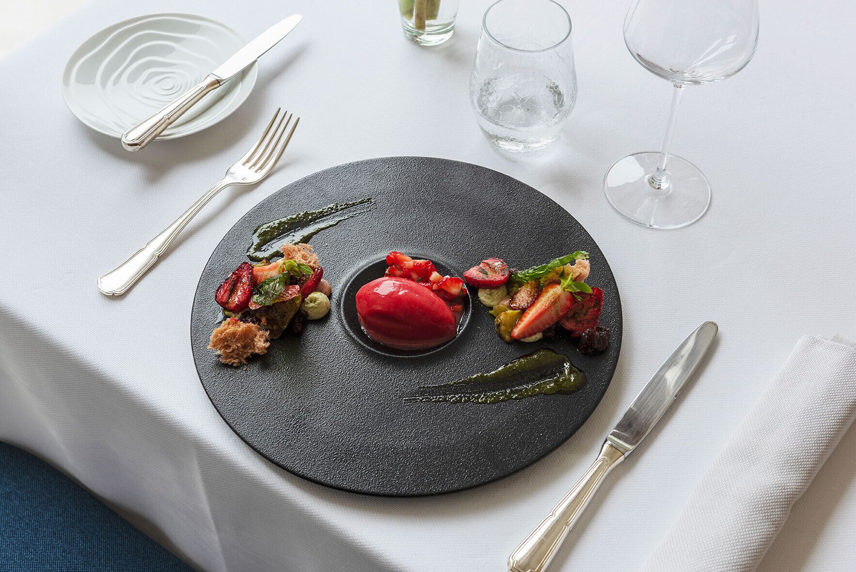 A black plate with a dessert and vegetables on a white tablecloth.