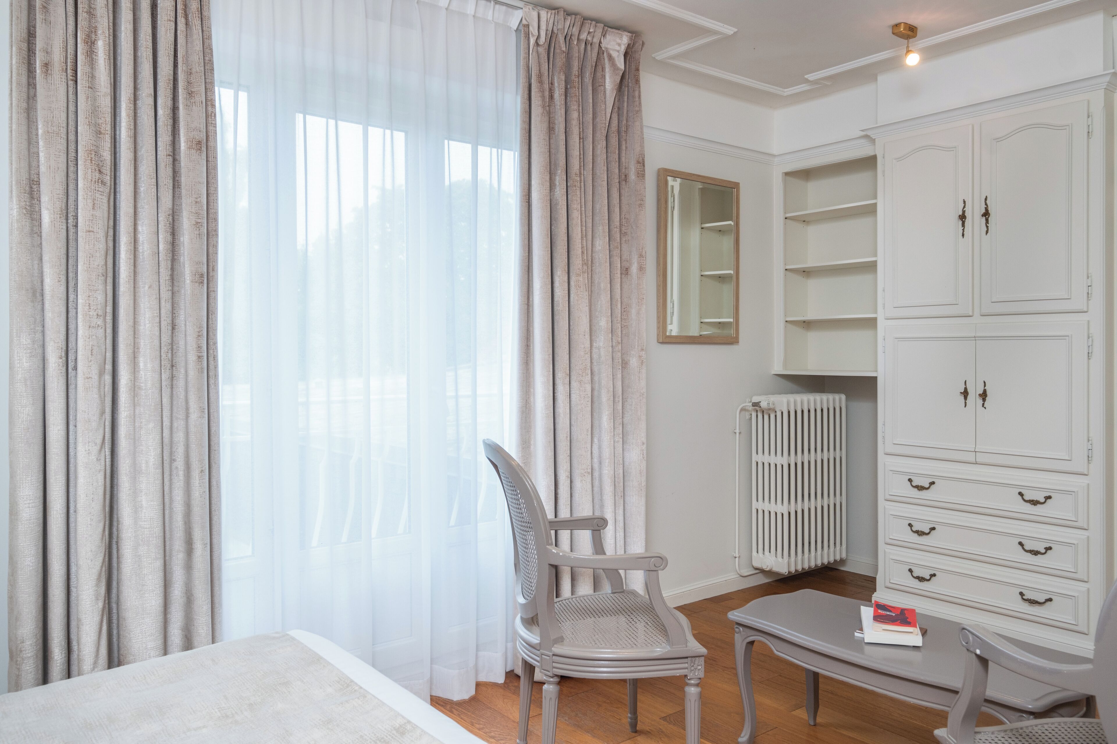 Una habitación con cama, una silla, una mesa, un armario y un radiador.