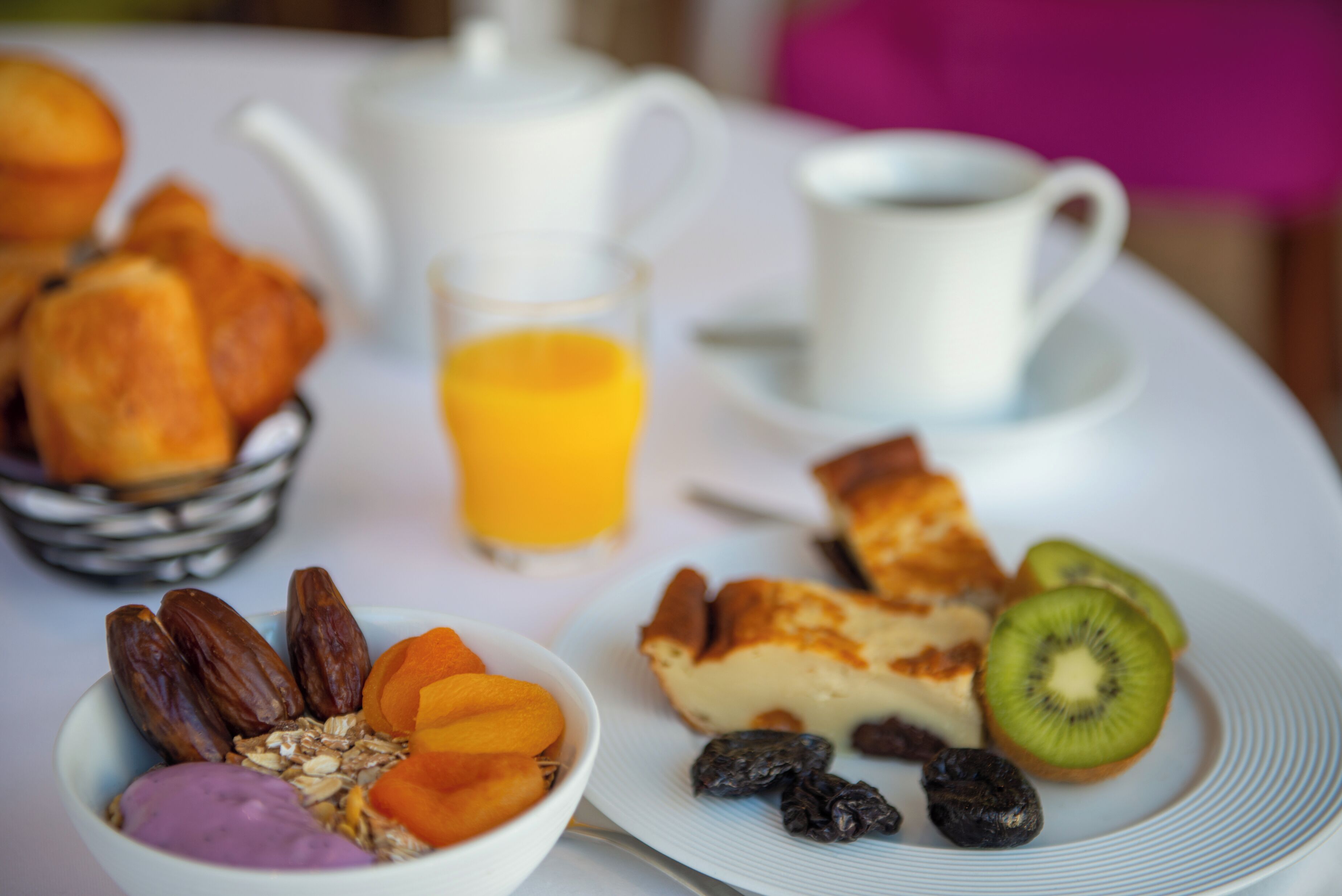 Una mesa de desayuno con una variedad de alimentos, incluyendo pasteles, frutas y un vaso de jugo de naranja.