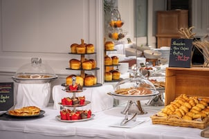 Una mesa de buffet con diversos productos horneados y repostería, incluyendo crepes pequeños, muffins y croissants.