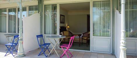 A covered patio with a table and chairs, a large window, and a door leading to an interior room.