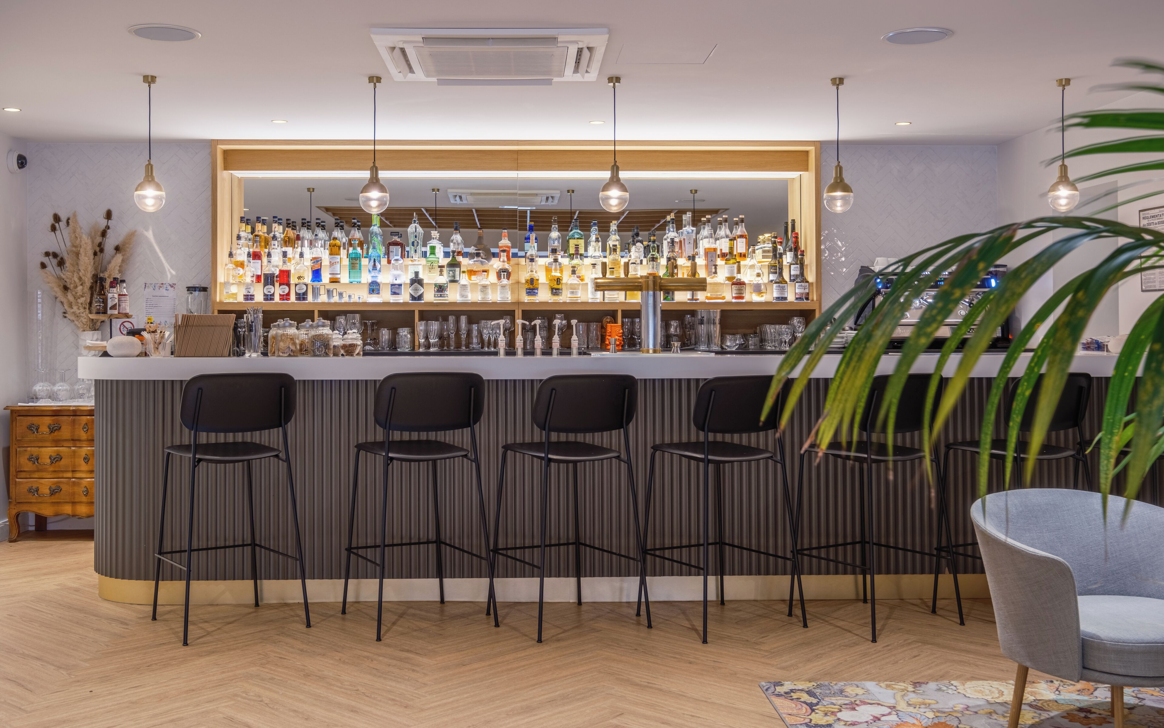 Un espace bar doté d’un comptoir en bois, de plusieurs tabourets et d’une variété de bouteilles et de verres.