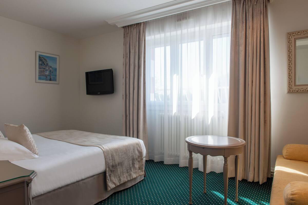 A hotel room with a bed, a small table, a TV, and a window with curtains.