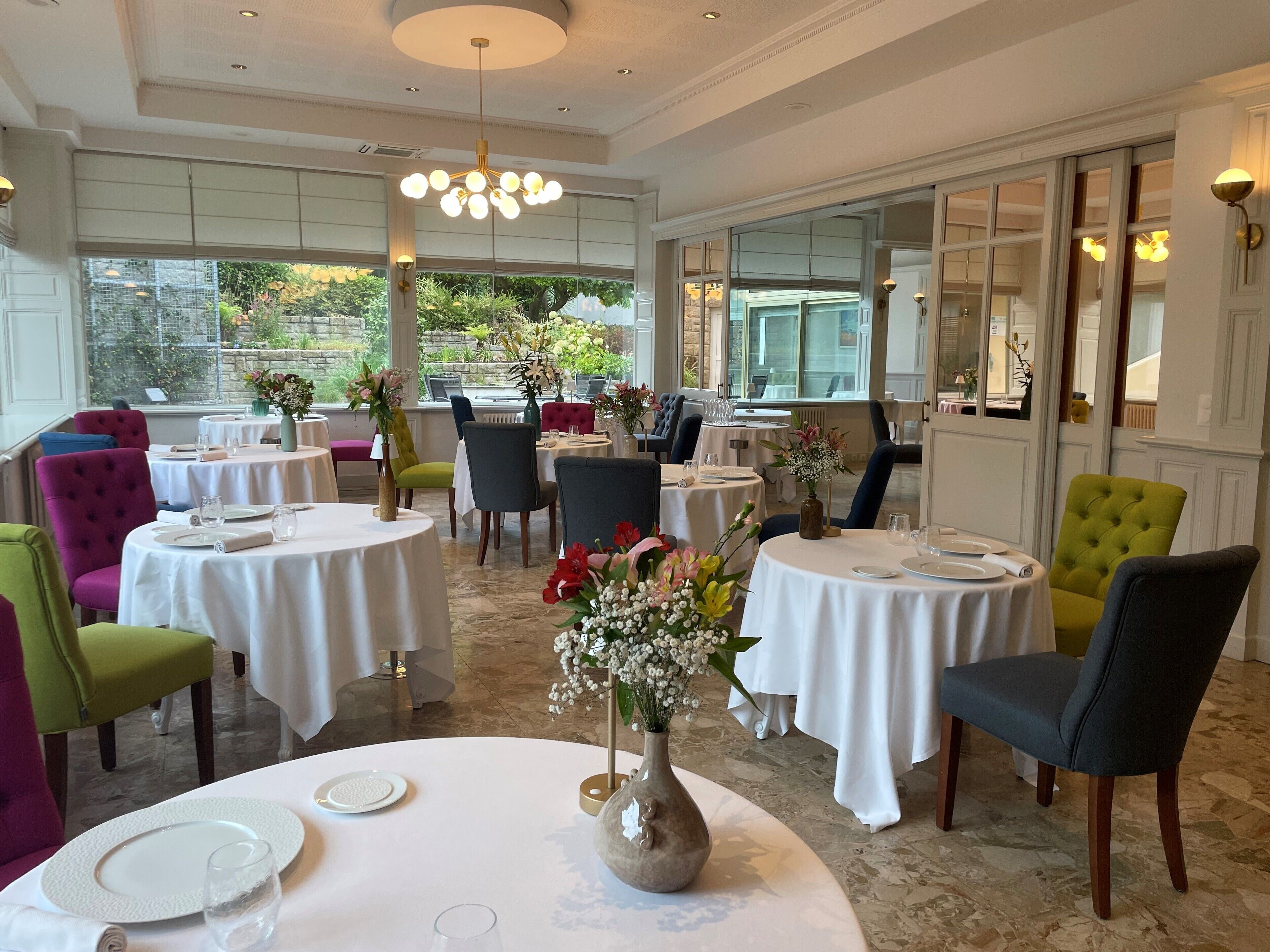 A restaurant with round tables, chairs, and flower centerpieces.
