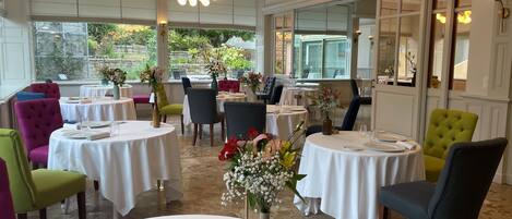 A restaurant with round tables, chairs, and flower centerpieces.