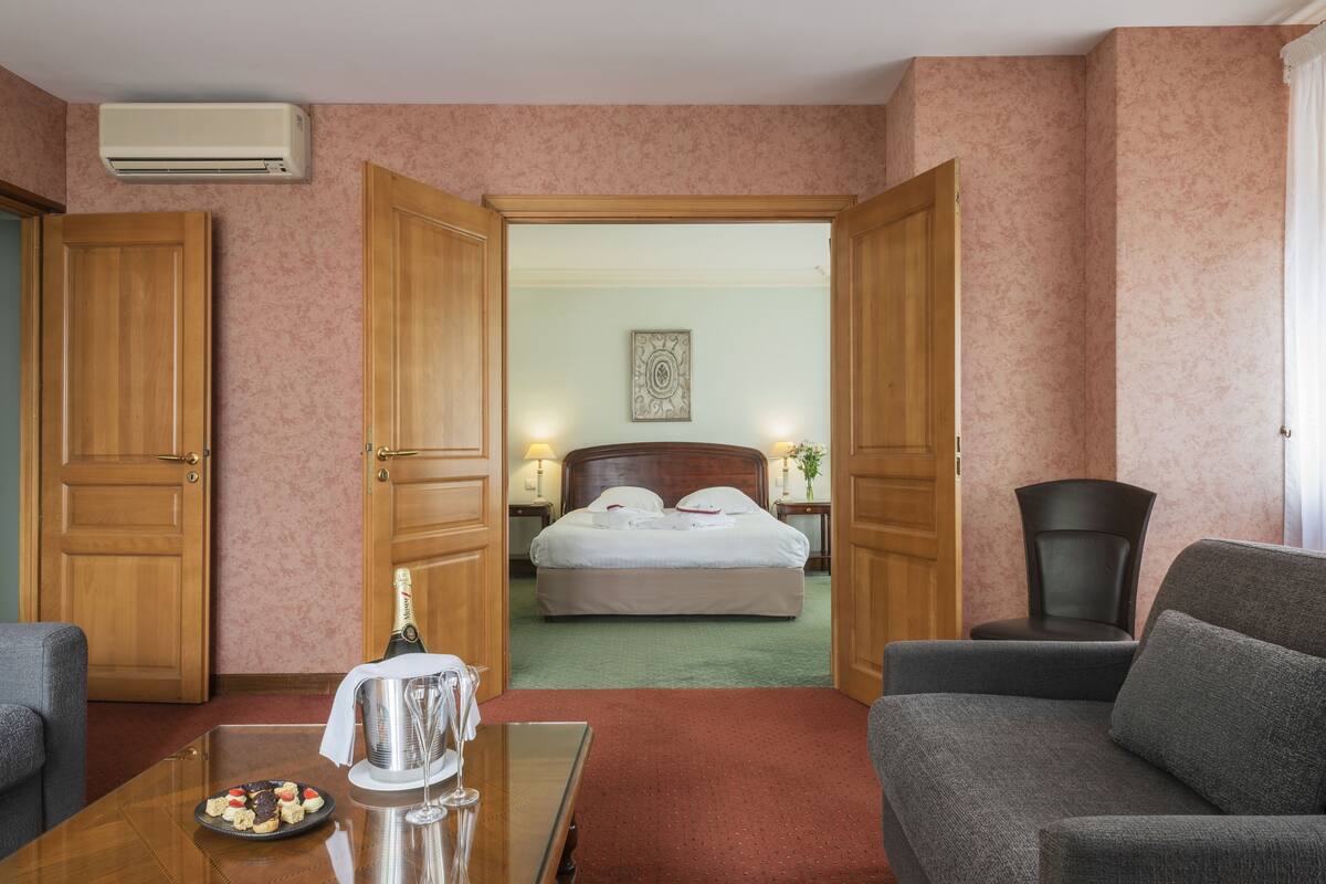 A hotel room with a bed, a desk with a plate of food, a chair, and an open door leading to another room.