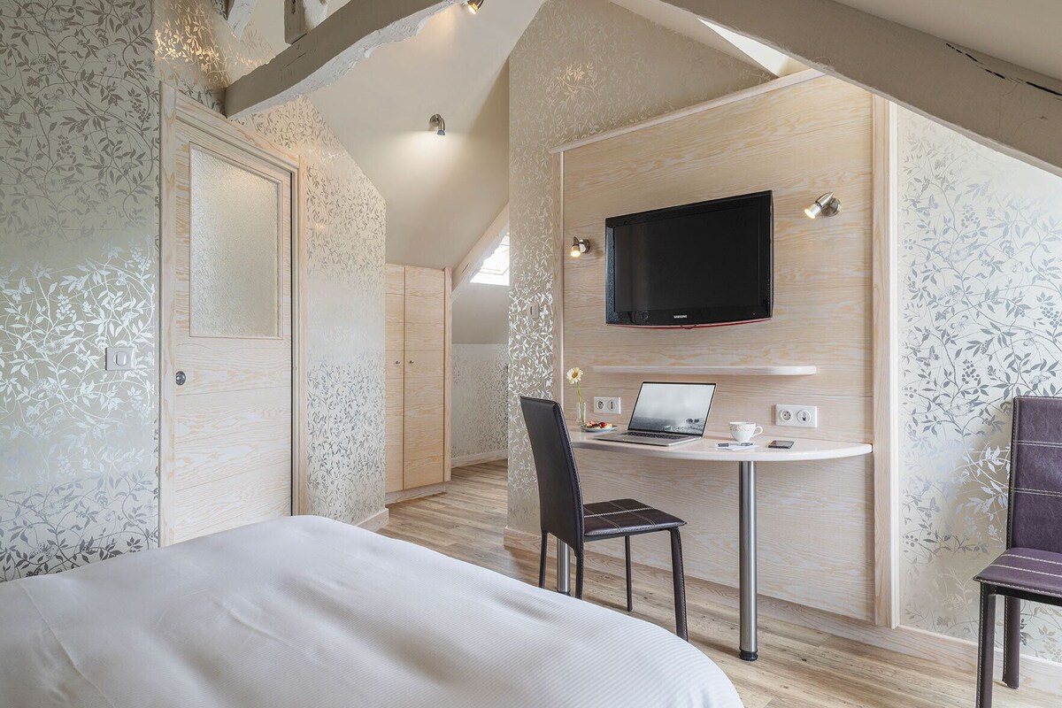A bedroom with a bed, a desk with a laptop, a chair, a TV, and a wardrobe.