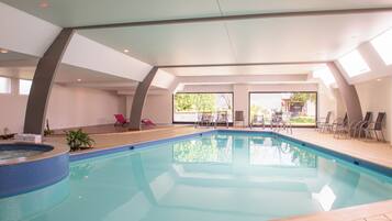 Una piscina interior con jacuzzi, zona de estar soleada y grandes ventanales.