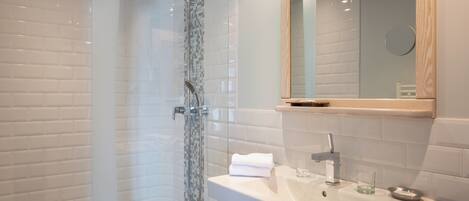 A modern bathroom with a glass-enclosed shower, a white sink with a mirror above it, and a small shelf with toiletries.