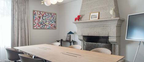 Une salle de conférence avec une longue table, des chaises, une cheminée, un téléviseur fixé au mur et un élément décoratif mural.