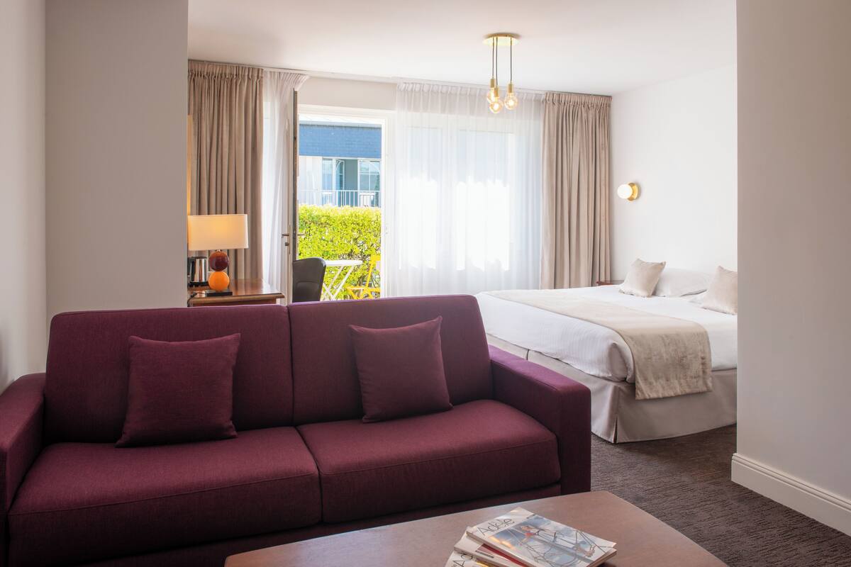A hotel room with a bed, a sofa, a coffee table, and a view of the outdoors.