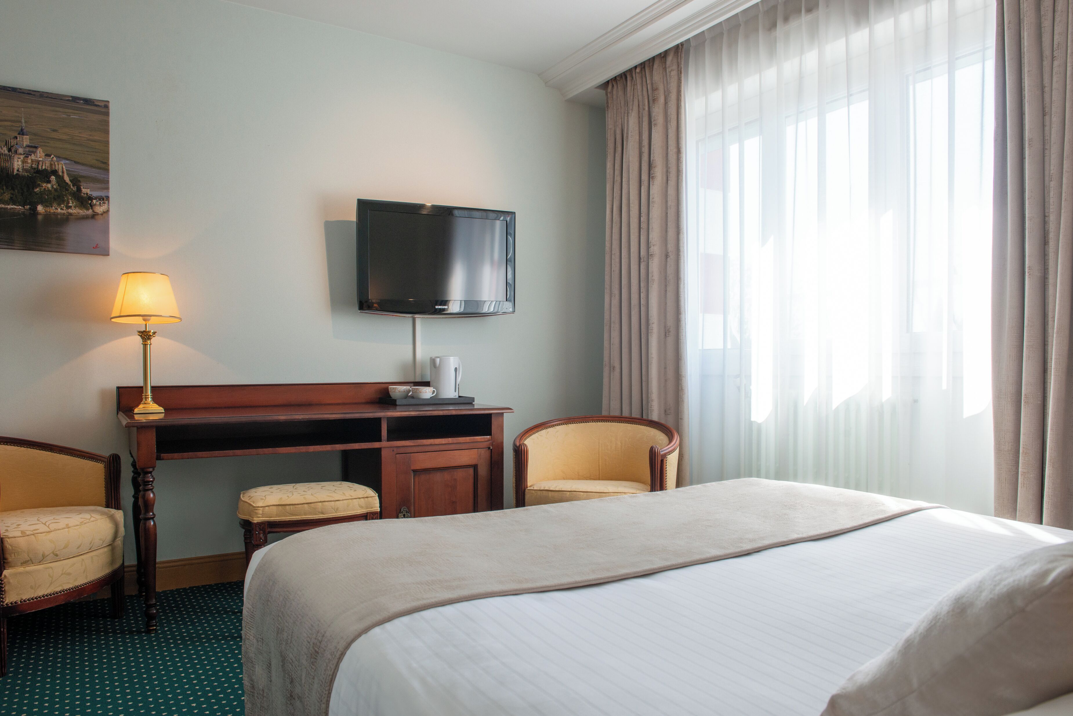 Quarto de hotel com uma cama grande, uma mesa com luminária, televisão e uma cadeira.