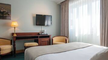 Quarto de hotel com uma cama grande, uma mesa com luminária, televisão e uma cadeira.