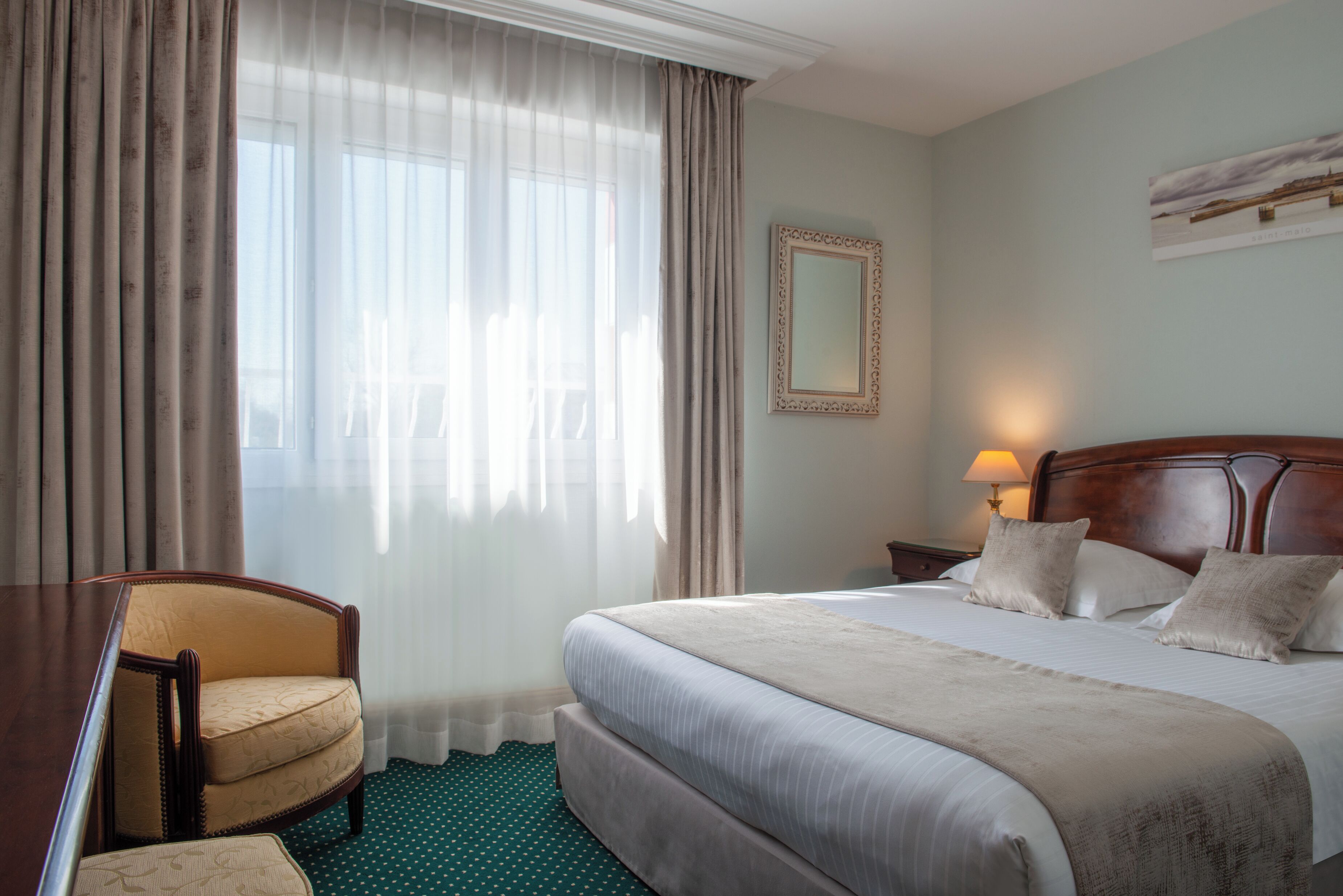 Une chambre d’hôtel avec un grand lit, une chaise, un bureau et une fenêtre avec des rideaux.
