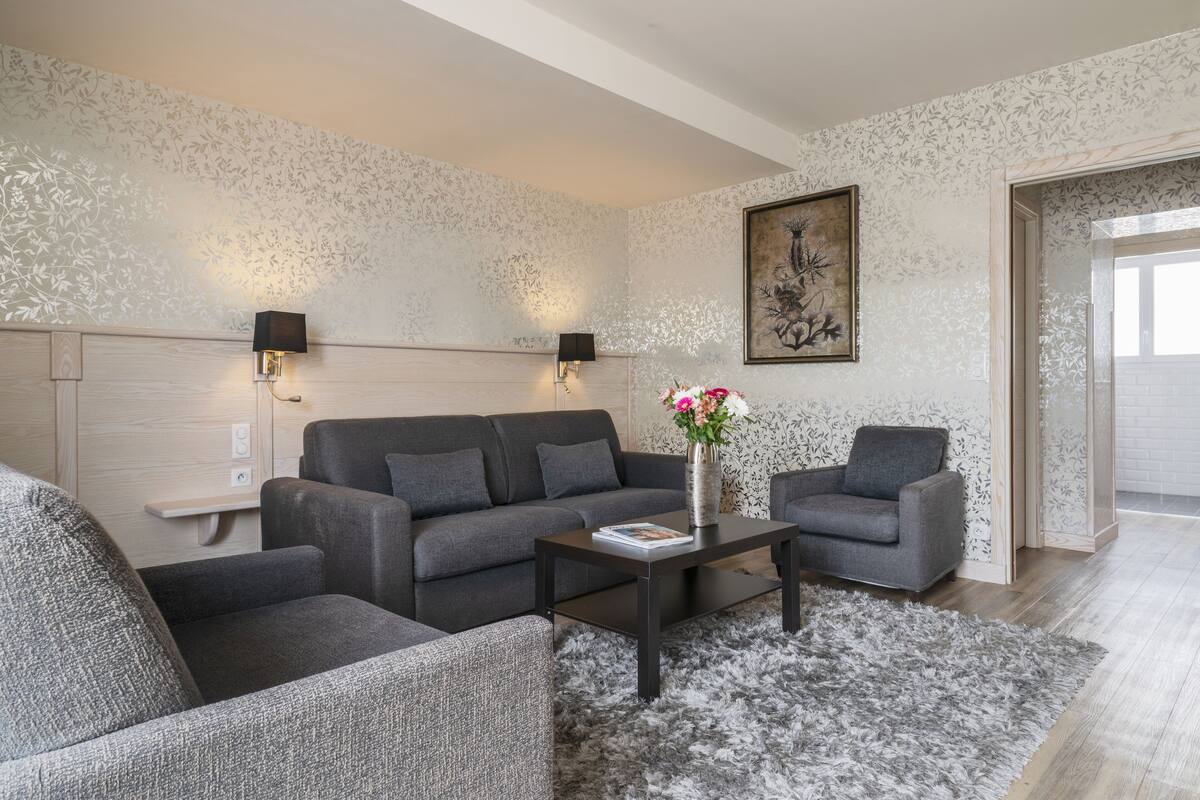 A modern living room with a grey sofa, a matching armchair, a coffee table, and a decorative vase with flowers.