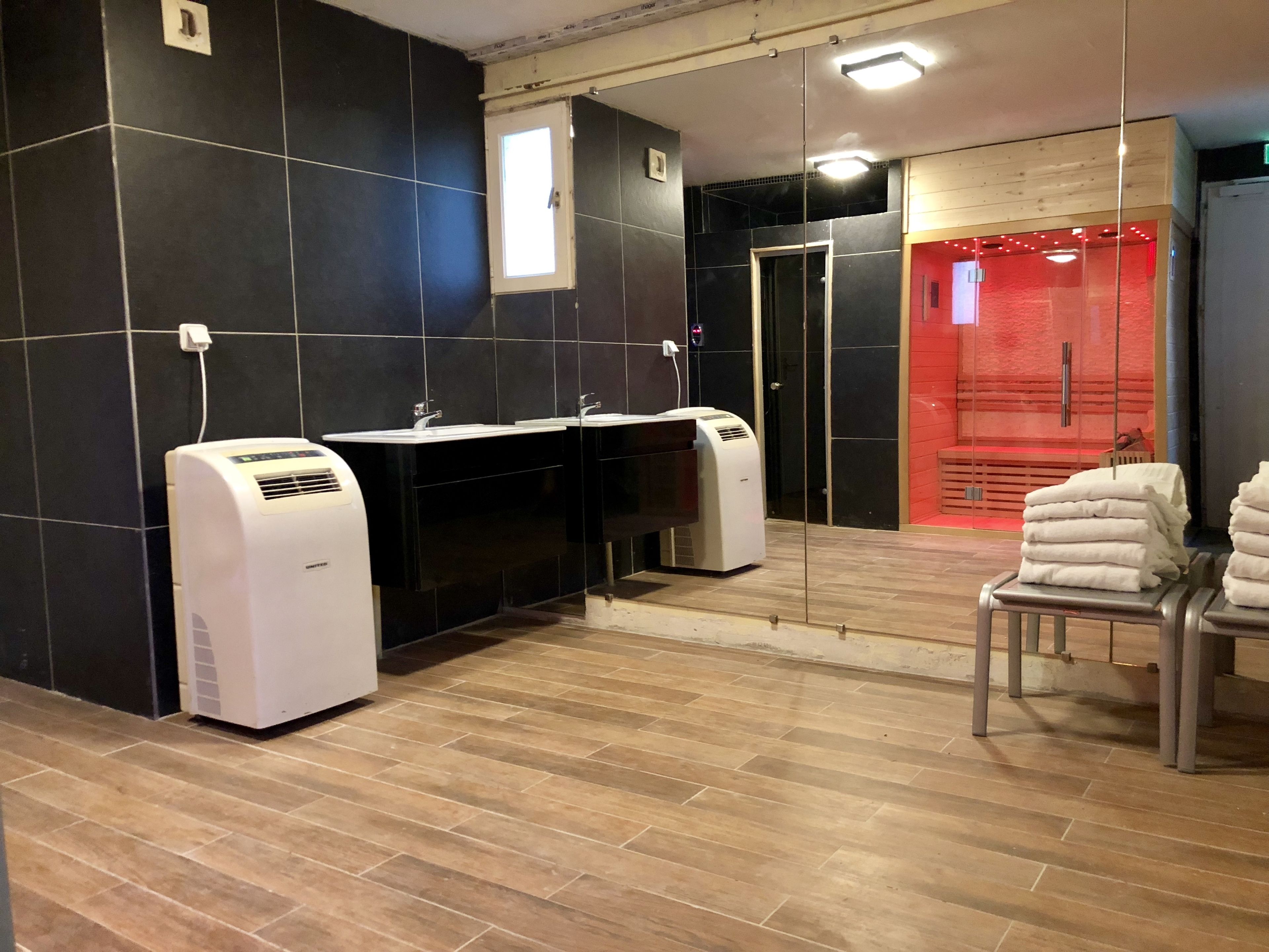 Um banheiro moderno com paredes revestidas de azulejos preto e branco, piso de madeira e área de sauna vermelha.