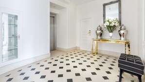 A hallway with a checkered floor, a glass display cabinet, a gold console table with a mirror, and a black and white bench. - Château de Sancy (Sancy)