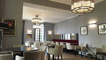 Interior de un restaurante con varias mesas y sillas, iluminación colgante y obras de arte enmarcadas en las paredes.