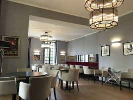 Interior de un restaurante con varias mesas y sillas, iluminación colgante y obras de arte enmarcadas en las paredes.