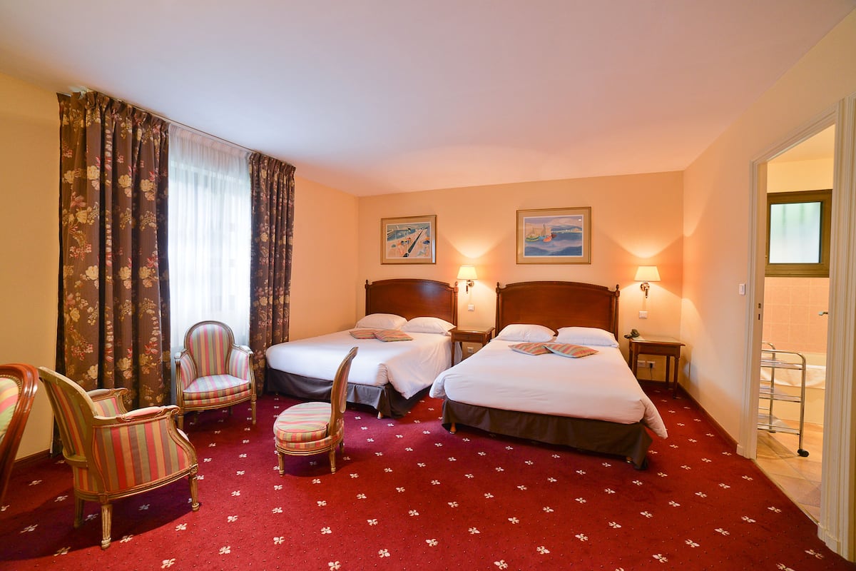 Hotellihuone, jossa on kaksi sänkyä, oleskelualue tuoleineen ja näkymä merelle ikkunasta.