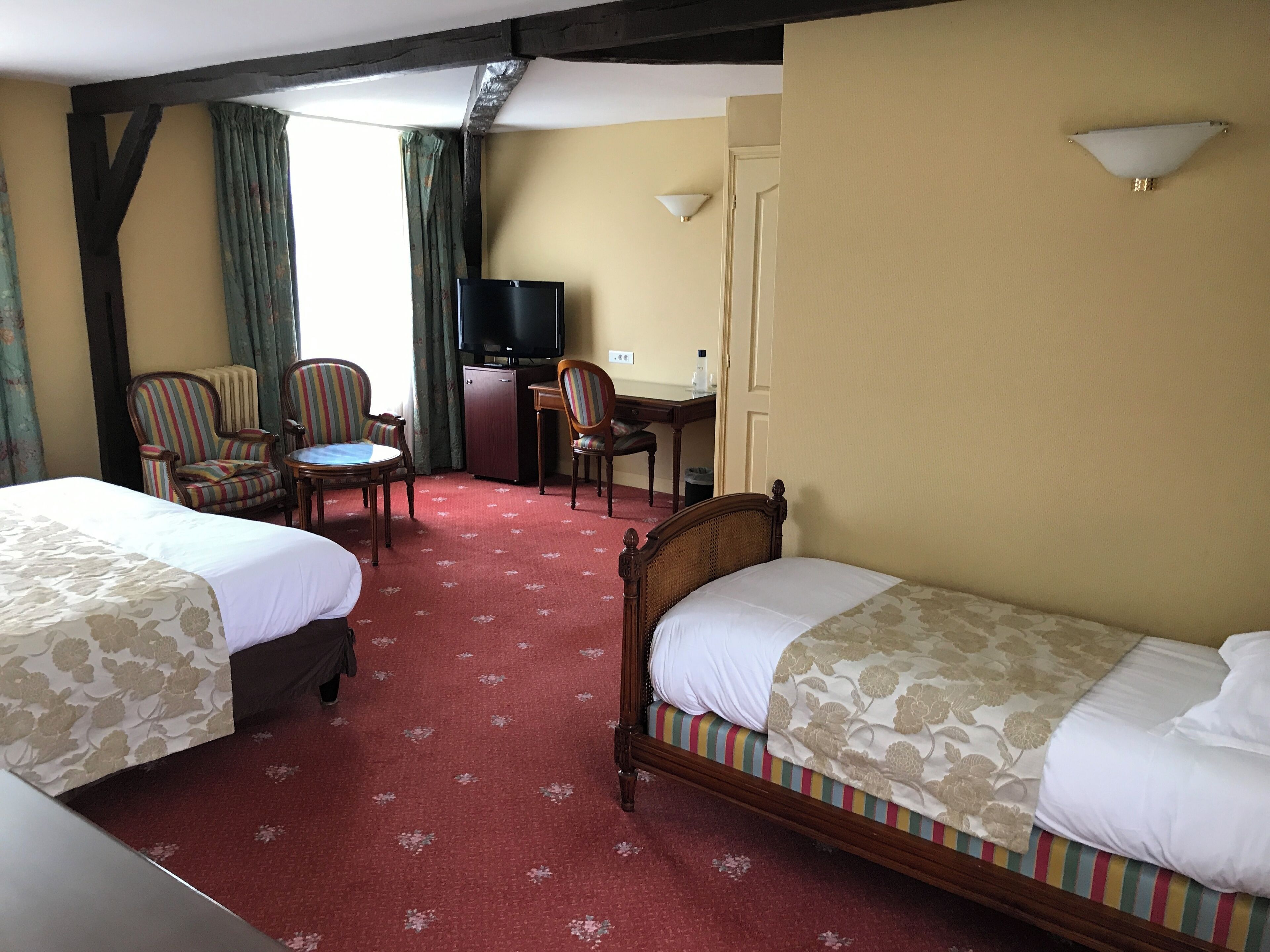 Habitación de hotel con dos camas, un escritorio, un televisor y dos sillones a rayas.