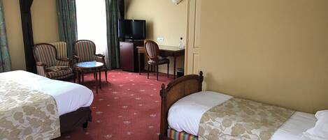 Habitación de hotel con dos camas, un escritorio, un televisor y dos sillones a rayas.