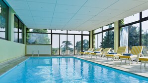 An indoor swimming pool with clear blue water, surrounded by large windows offering views of trees and a waterfall. - Château de Sancy (Sancy)