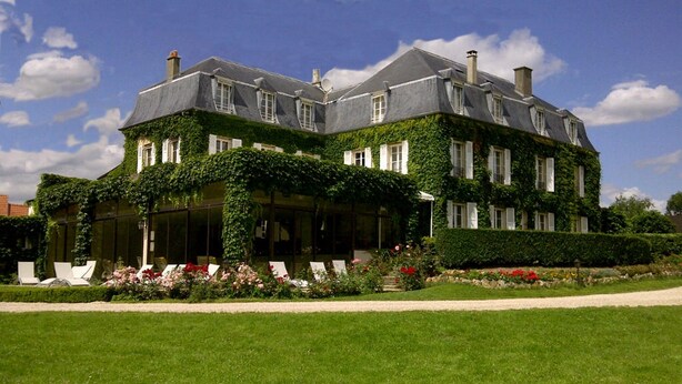 A large, ivy-covered building with a symmetrical facade, multiple windows, and a well-maintained garden with a lawn and flower beds. - Château de Sancy (Sancy)