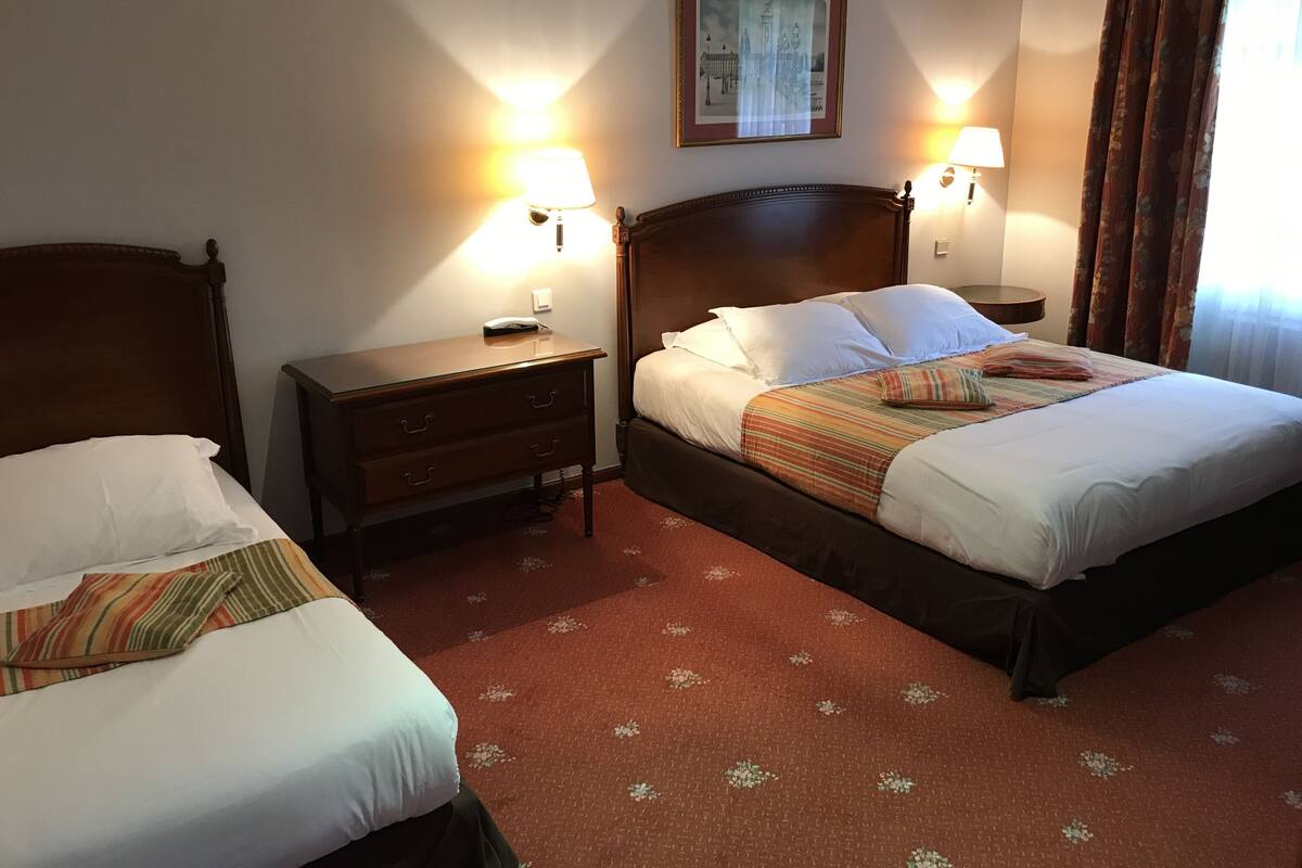 Hotellihuone, jossa on kaksi sänkyä, yöpöytä, lamppu ja seinällä oleva kehystetty kuva.