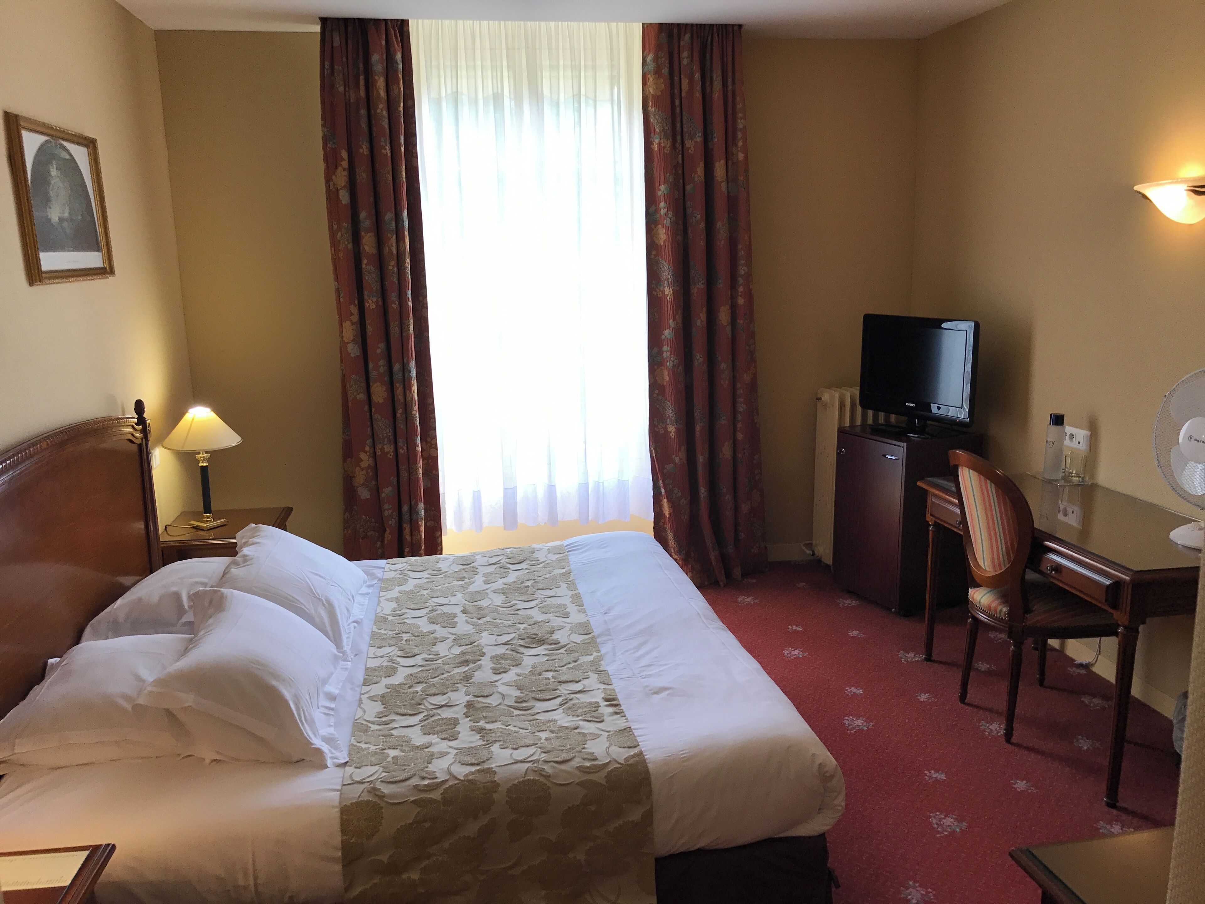 A hotel room with a bed, a desk, a chair, a television, and a lamp.
