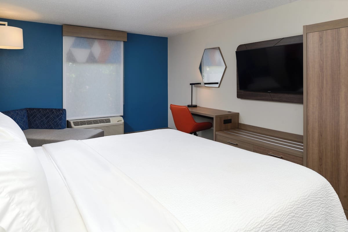 Habitación de hotel con una cama grande, un escritorio con silla, un televisor de pantalla plana y una ventana con persianas.
