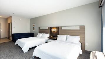 A hotel room with two beds, a sofa, a wall-mounted light, and a large window.