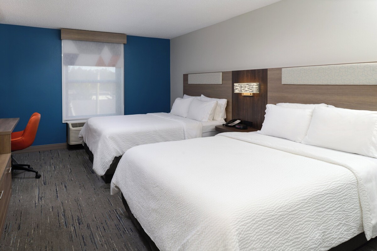 A hotel room with two beds, a desk, and a chair.