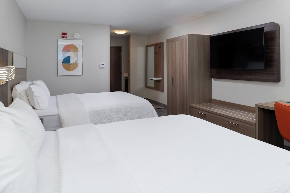 Una habitación de hotel con dos camas, un televisor fijado a la pared, un armario de madera y un escritorio pequeño con una silla.