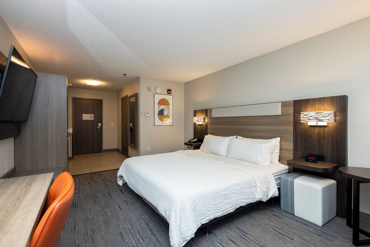 Une chambre d’hôtel avec un lit, une table de chevet, une chaise et un téléviseur fixé au mur gauche.
