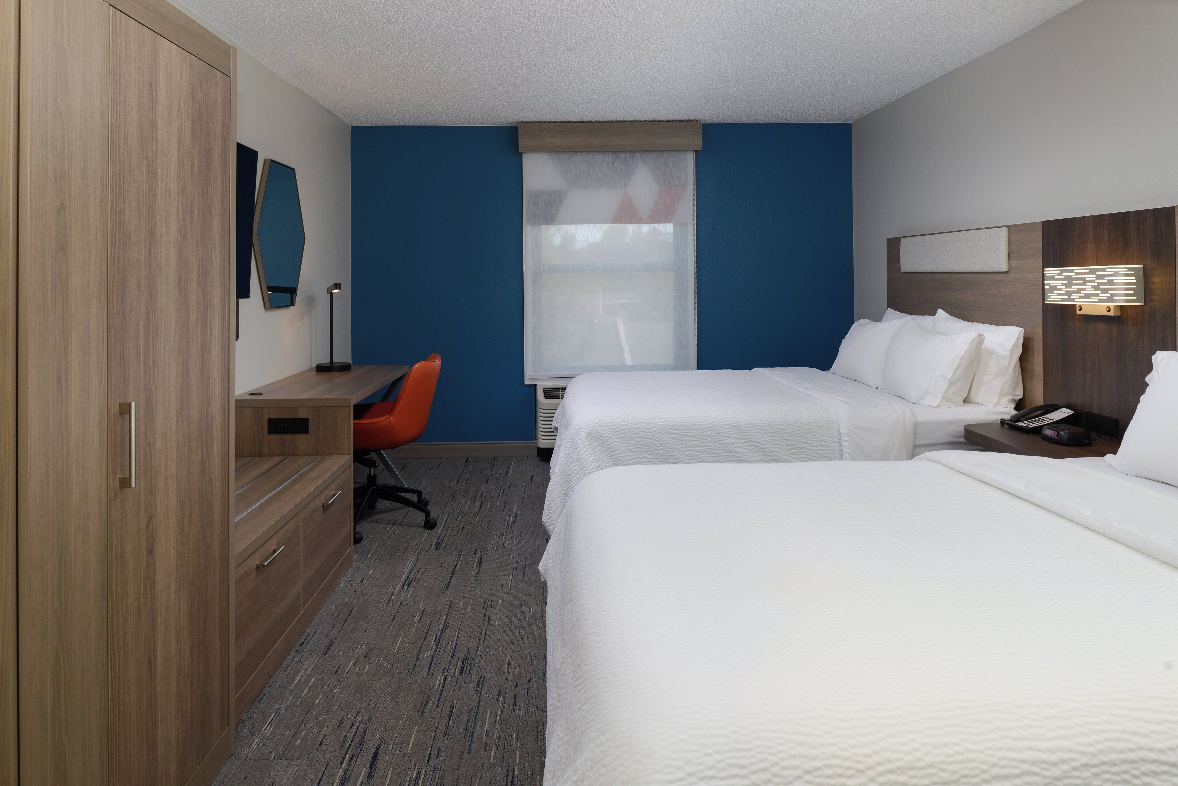A hotel room with two beds, a desk, a chair, and a wardrobe.