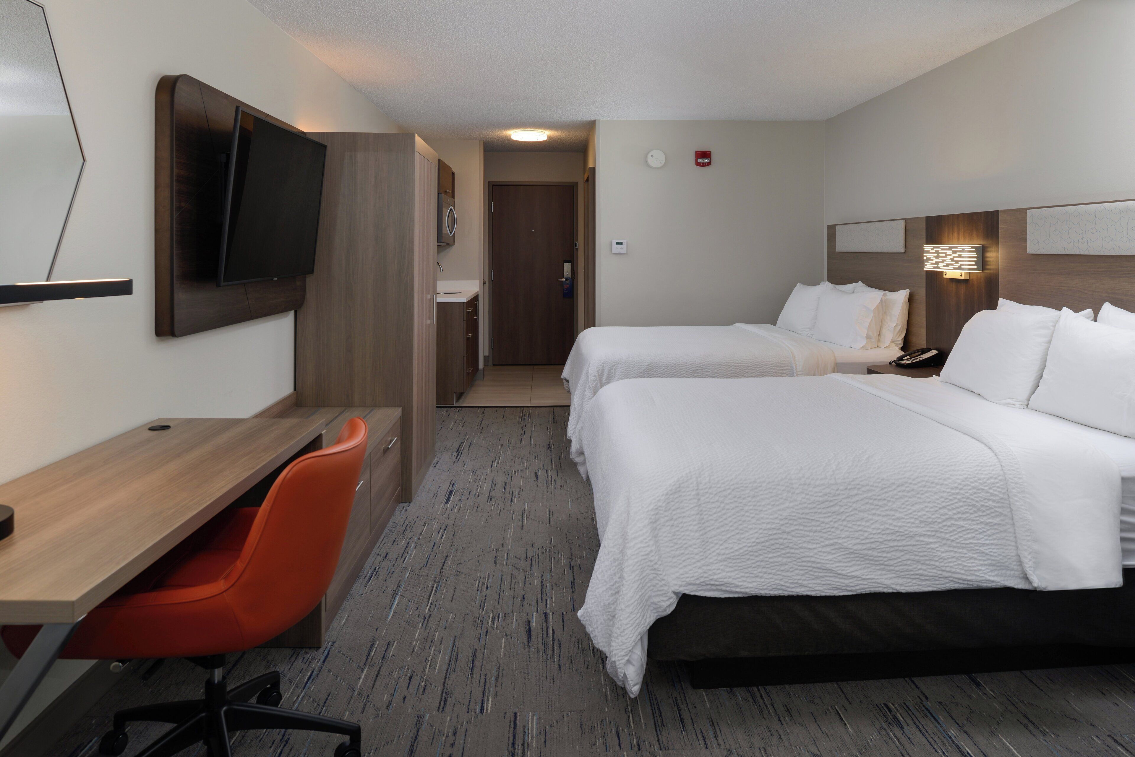 Een hotelkamer met twee bedden, een bureau, een stoel, een televisie en een deur naar de badkamer.