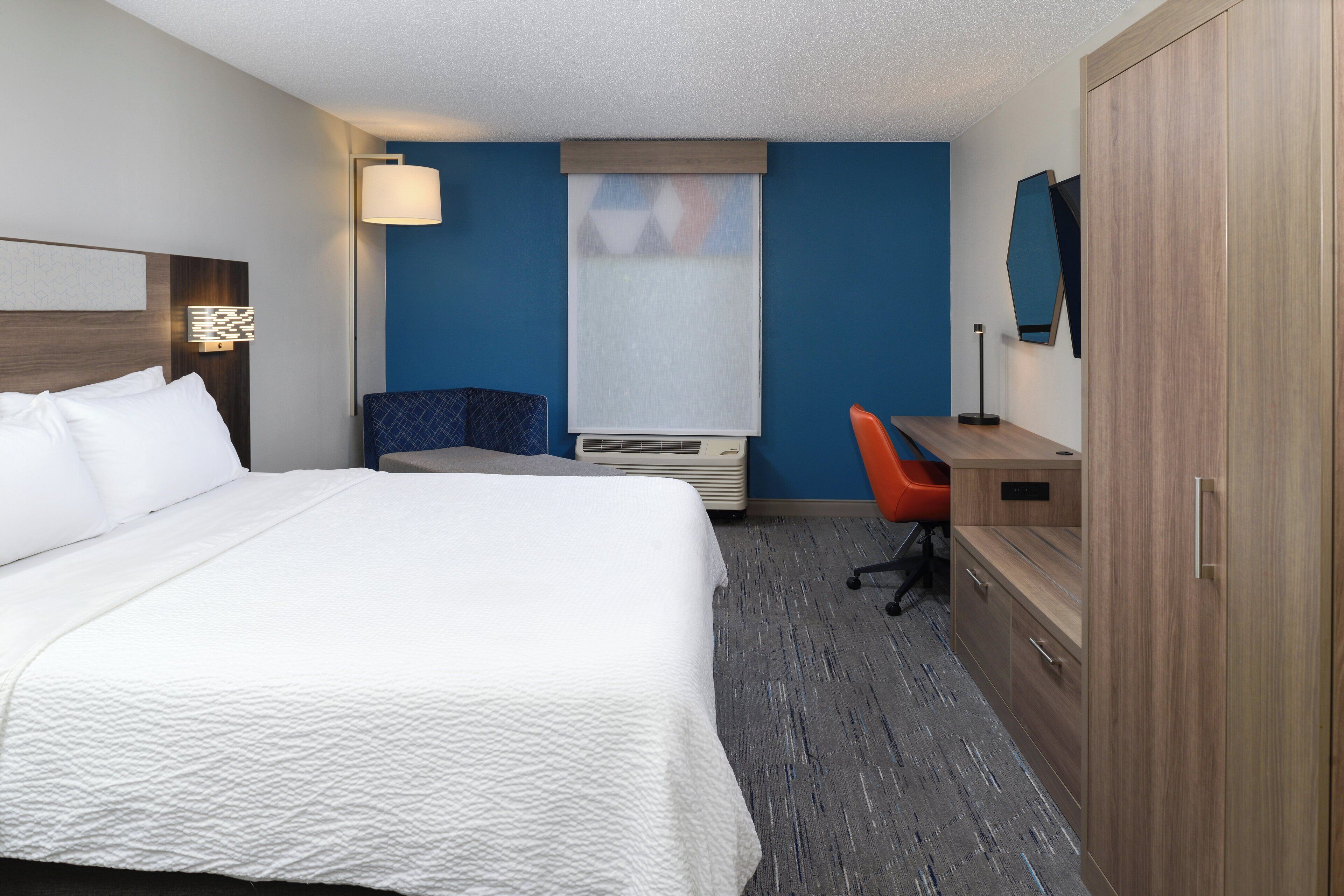 Une chambre d’hôtel avec un grand lit, un bureau, une chaise, une armoire et un téléviseur fixé au mur.