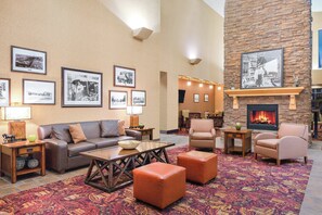 A hotel lobby with a fireplace, framed historical photographs, a sofa, armchairs, and a patterned carpet.