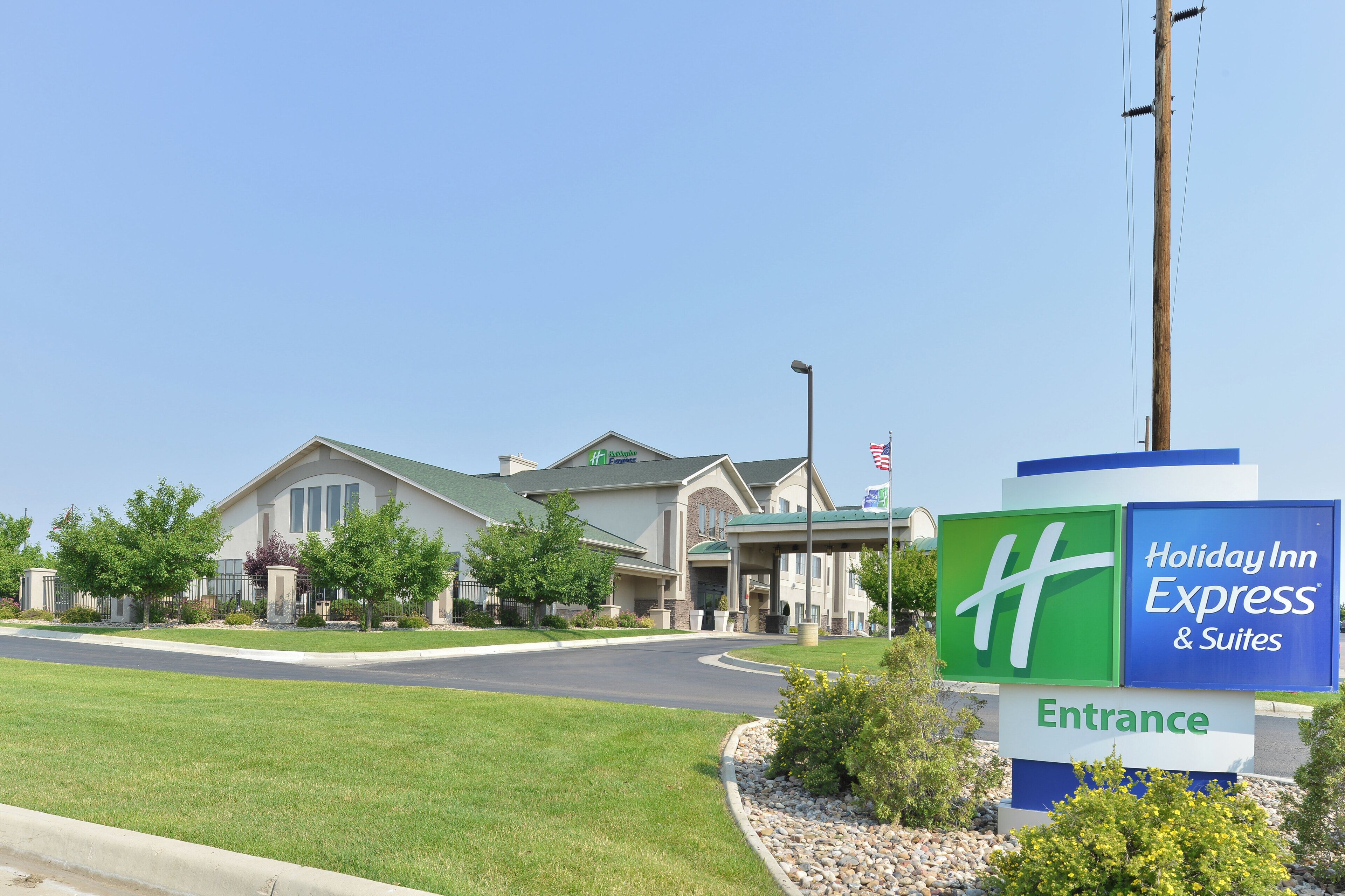 Edifici d'Holiday Inn Express & Suites amb un cartell d'entrada ben visible, envoltat de jardineria cuidada.