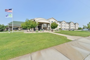 A multi-story hotel with a central entrance, a flagpole with flags, and a well-maintained lawn.