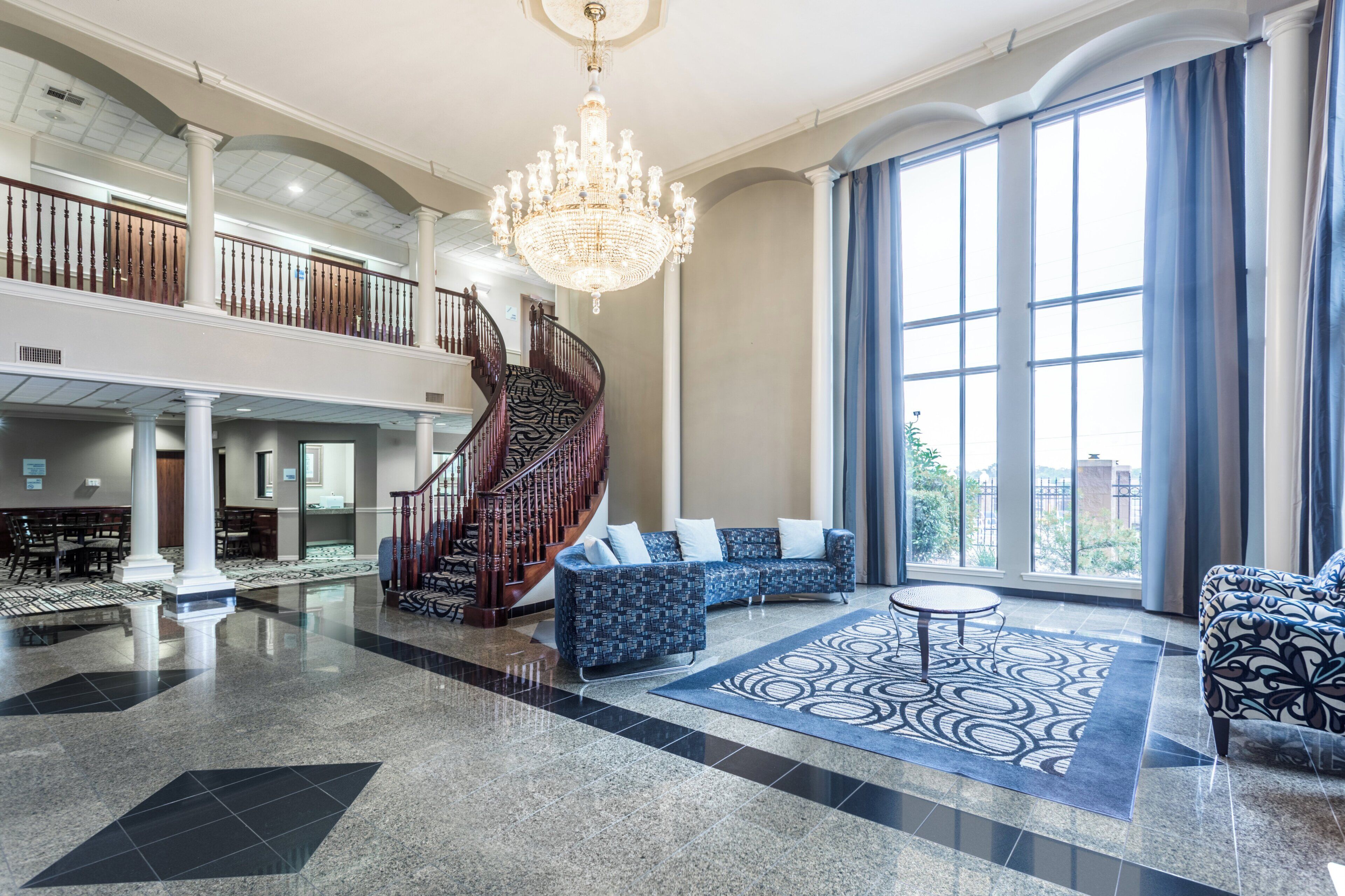 A spacious lobby with a grand staircase, a chandelier, and a large window with curtains.
