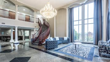 A spacious lobby with a grand staircase, a chandelier, and a large window with curtains.