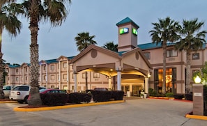 A hotel with a prominent clock tower, a covered entrance, and a parking lot with several cars. - Holiday Inn Express Hotel & Suites Lake Charles by IHG (Lake Charles)
