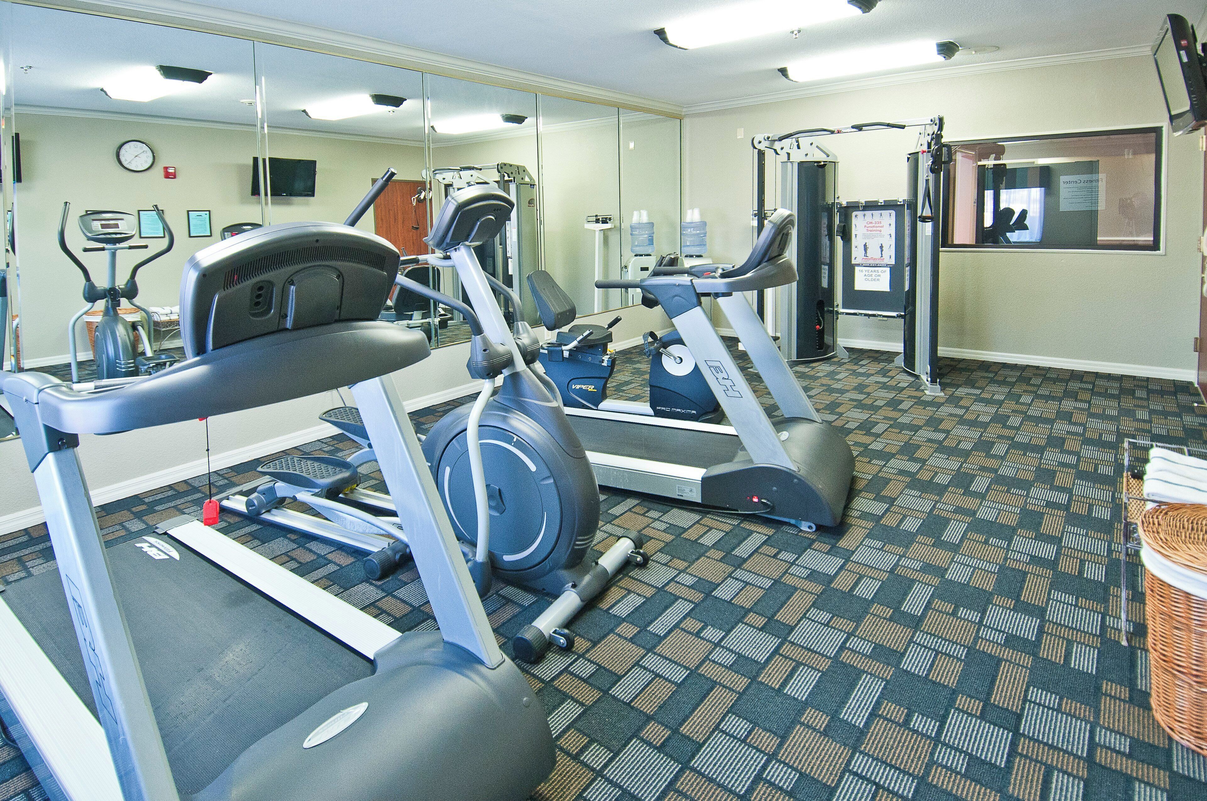 Une salle de sport équipée de tapis de course, de vélos d’appartement et d’un mur recouvert de miroirs.