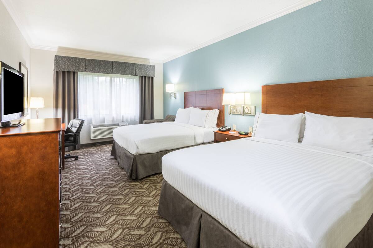 Une chambre d’hôtel avec deux lits, un bureau, une télévision et une fenêtre avec des rideaux.