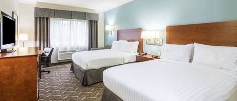 A hotel room with two beds, a desk, a TV, and a window with curtains.