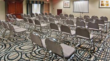 Un salón de conferencias con hileras de sillas, una pantalla de proyector y una alfombra con diseño circular.