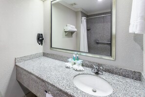 A bathroom with a granite countertop, a sink, a mirror, a towel rack, and a shower area. - Holiday Inn Express Hotel & Suites Lake Charles by IHG (Lake Charles)