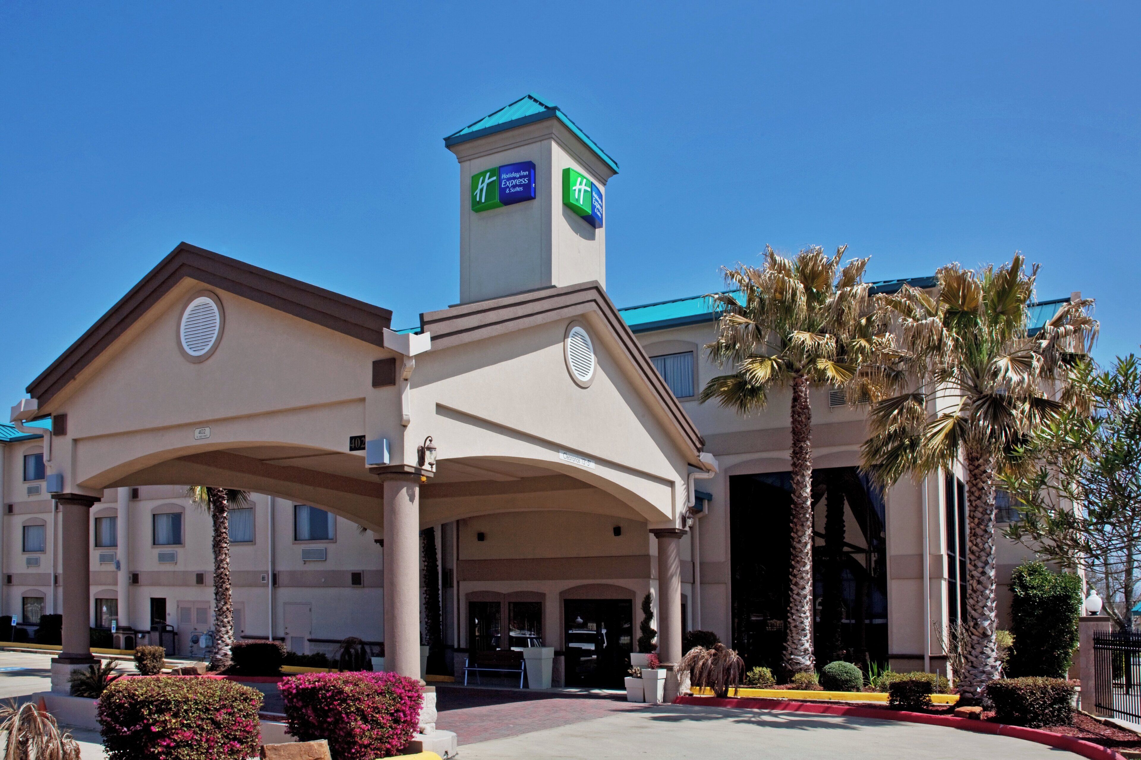 A Holiday Inn Express building with a central entrance, palm trees, and a clear blue sky.
